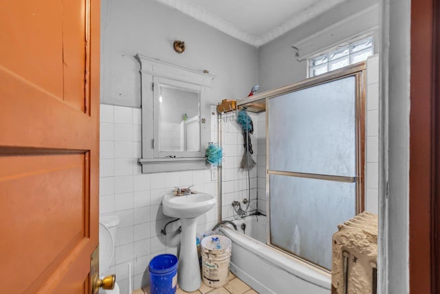 bathroom with tile walls and bath / shower combo with glass door