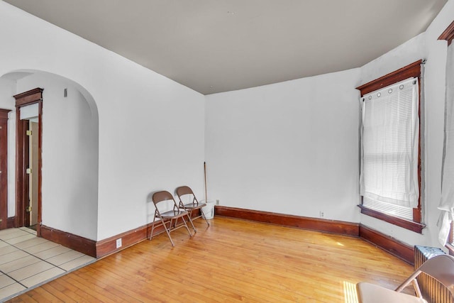 unfurnished room with baseboards, arched walkways, and wood-type flooring