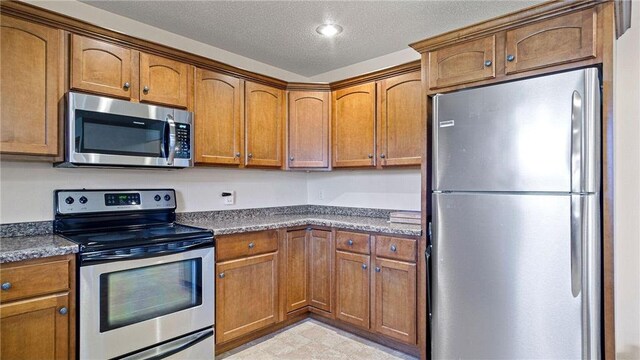 kitchen with dark countertops, brown cabinetry, appliances with stainless steel finishes, and a textured ceiling