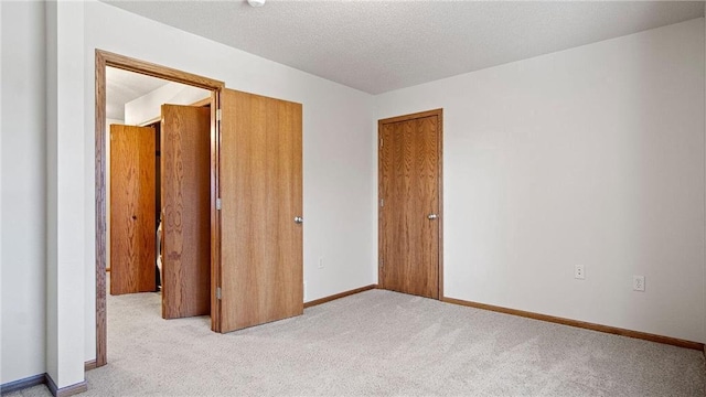 unfurnished bedroom with light carpet, a closet, a textured ceiling, and baseboards