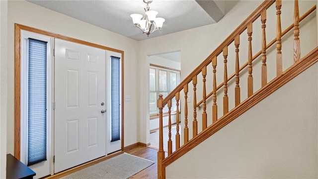 entryway with a textured ceiling, wood finished floors, an inviting chandelier, baseboards, and stairs