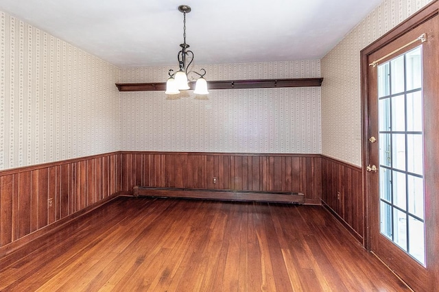 empty room with dark wood-type flooring, wainscoting, wallpapered walls, baseboard heating, and a chandelier