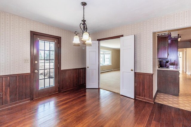 unfurnished dining area with wallpapered walls, hardwood / wood-style flooring, a baseboard heating unit, and wainscoting