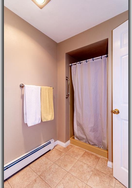 full bathroom with a baseboard heating unit, tile patterned floors, baseboards, and a shower with shower curtain