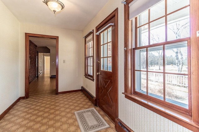 hallway with wallpapered walls, light floors, and baseboards