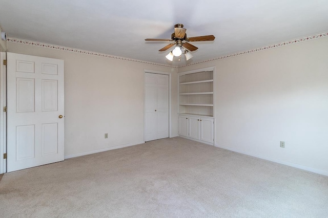 unfurnished room with built in features, baseboards, light colored carpet, and a ceiling fan