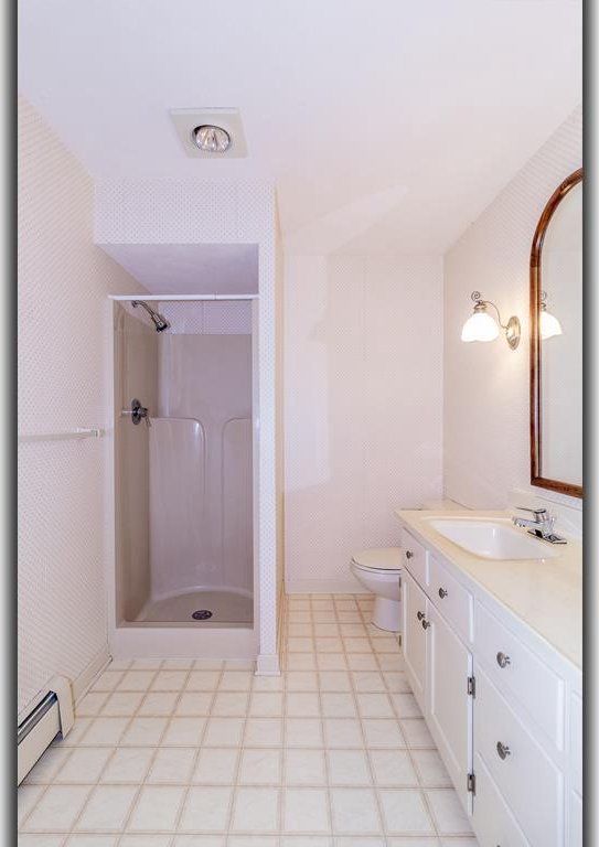 full bath featuring a shower stall, toilet, vanity, and a baseboard radiator