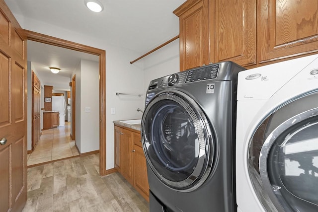 laundry room featuring washer and dryer, baseboards, cabinet space, and light wood-style floors