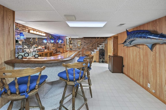 bar with visible vents, a paneled ceiling, a bar, and wooden walls