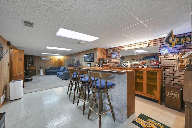 bar with wooden walls, light floors, visible vents, a paneled ceiling, and a dry bar