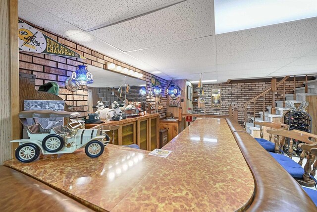 bar featuring stairs, brick wall, and a drop ceiling