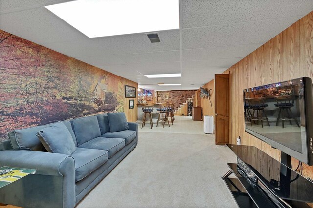 living room with light colored carpet, a bar, a paneled ceiling, and wood walls