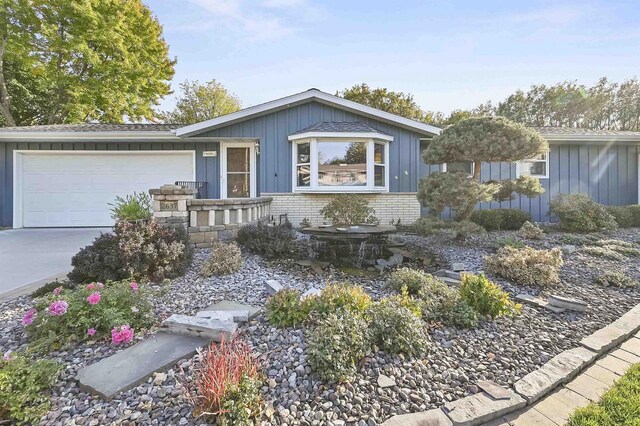 single story home with board and batten siding, concrete driveway, a garage, and brick siding