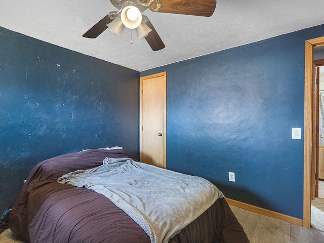 bedroom featuring a ceiling fan, wood finished floors, baseboards, a textured ceiling, and a textured wall