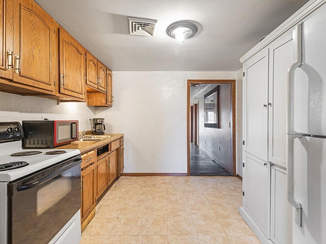 kitchen with baseboards, visible vents, electric range, freestanding refrigerator, and brown cabinets