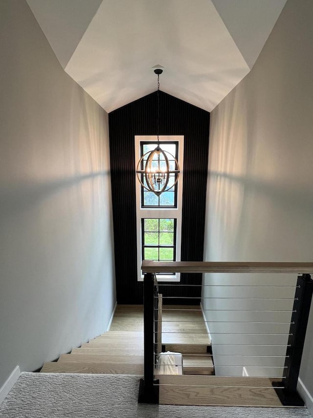 stairs with a chandelier, lofted ceiling, and wood finished floors