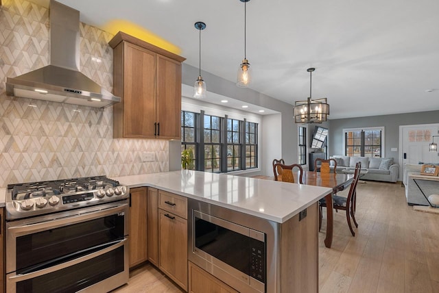 kitchen with stainless steel appliances, light wood-style floors, open floor plan, and wall chimney range hood