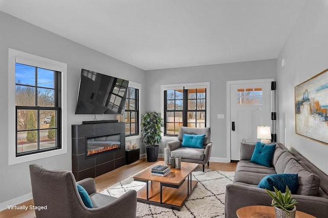 living room featuring a glass covered fireplace, wood finished floors, and baseboards