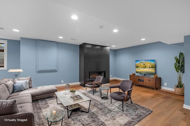 living area with light wood finished floors, recessed lighting, a large fireplace, and baseboards