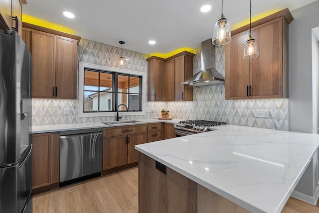 kitchen with a sink, light wood-style floors, a peninsula, appliances with stainless steel finishes, and wall chimney exhaust hood