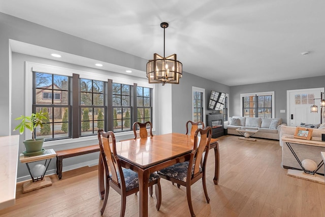 dining space with baseboards, an inviting chandelier, recessed lighting, a glass covered fireplace, and light wood-type flooring