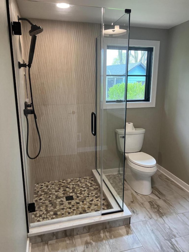 bathroom with marble finish floor, a stall shower, toilet, and baseboards