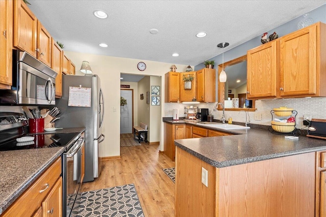 kitchen with light wood-style flooring, a sink, decorative backsplash, appliances with stainless steel finishes, and dark countertops