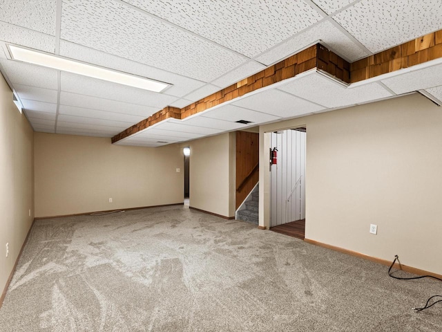 finished below grade area with carpet flooring, stairs, baseboards, and a drop ceiling