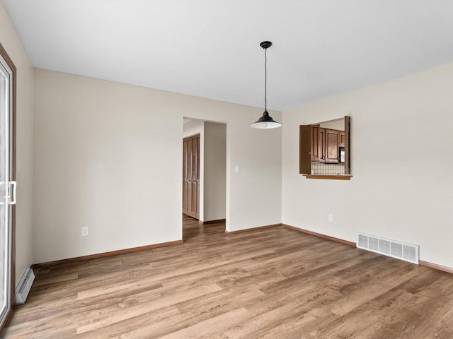 empty room featuring visible vents, baseboards, light wood-style floors, and a baseboard radiator