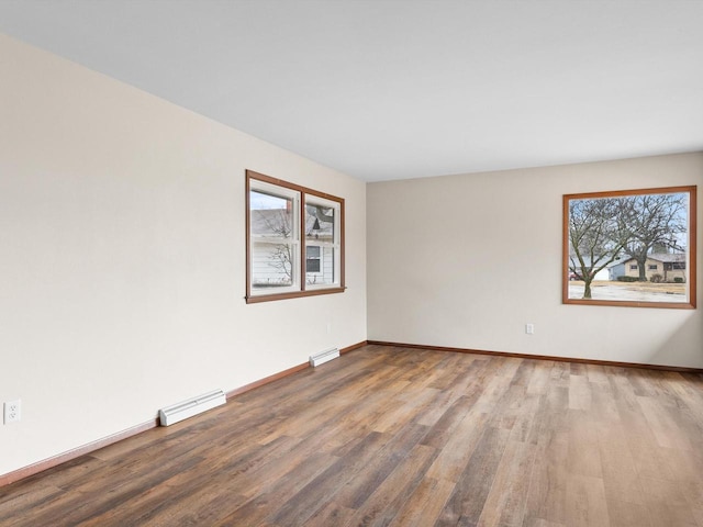 empty room featuring baseboard heating, visible vents, baseboards, and wood finished floors