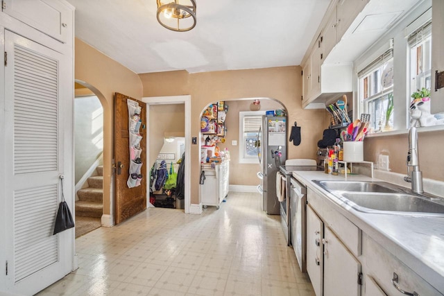 kitchen with light floors, baseboards, arched walkways, a sink, and light countertops