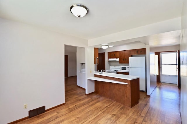 kitchen featuring visible vents, white appliances, a peninsula, exhaust hood, and light countertops