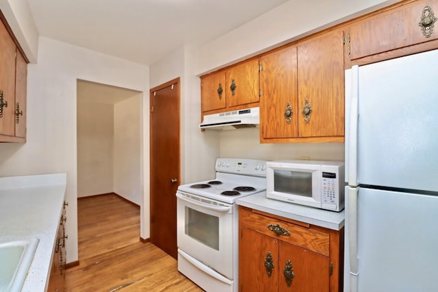 kitchen with under cabinet range hood, white appliances, light wood finished floors, and light countertops