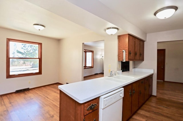 kitchen featuring a sink, dishwasher, wood finished floors, and light countertops