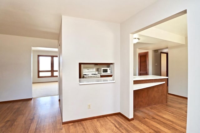 interior space with baseboards, white appliances, wood finished floors, and light countertops