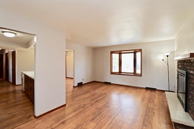 unfurnished living room featuring a brick fireplace, wood finished floors, and baseboards