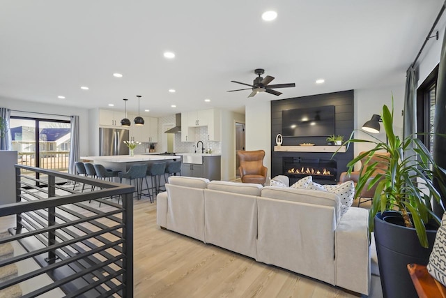 living room with recessed lighting, a large fireplace, and light wood-style flooring