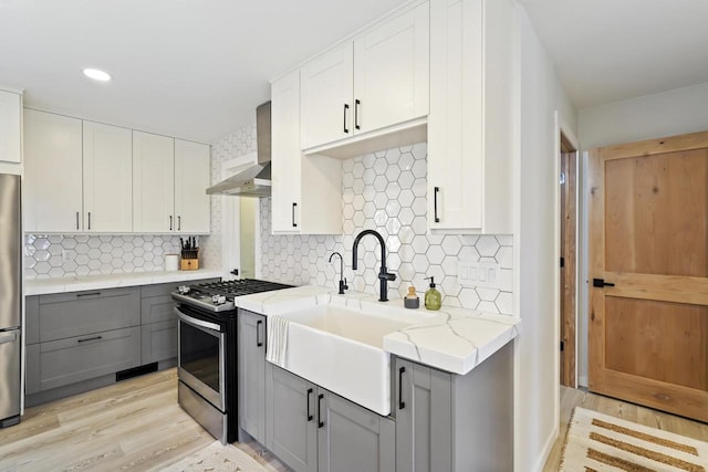 kitchen featuring light wood finished floors, gray cabinetry, light stone counters, appliances with stainless steel finishes, and a sink