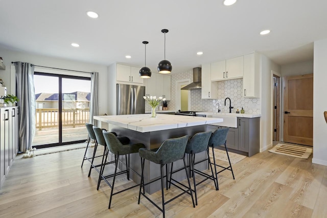 kitchen featuring light wood-type flooring, a kitchen island, appliances with stainless steel finishes, wall chimney exhaust hood, and decorative backsplash