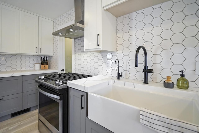 kitchen with visible vents, gray cabinets, a sink, stainless steel range with gas cooktop, and wall chimney exhaust hood