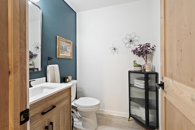 half bath featuring baseboards, toilet, wood finished floors, and vanity