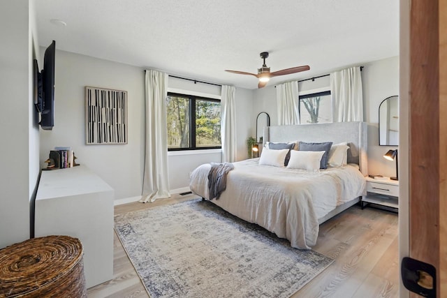 bedroom with a textured ceiling, a ceiling fan, baseboards, and wood finished floors