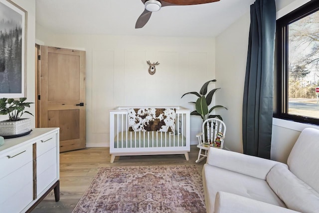 bedroom featuring ceiling fan, a nursery area, and wood finished floors