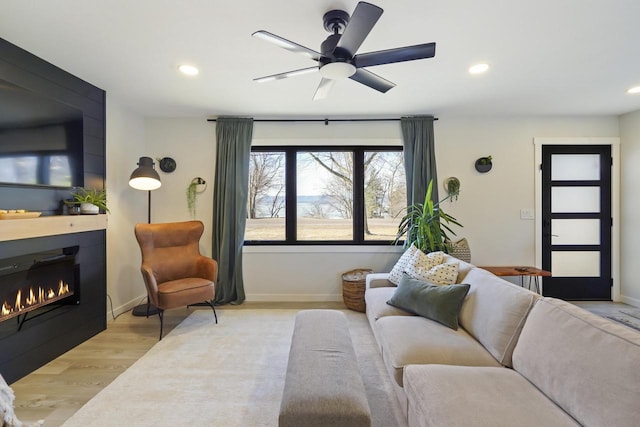 living room with a ceiling fan, wood finished floors, recessed lighting, a lit fireplace, and baseboards