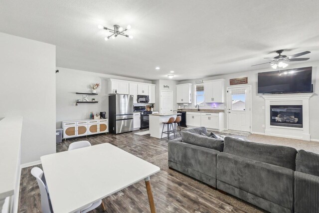 living area with ceiling fan, dark wood-style floors, baseboards, and a glass covered fireplace