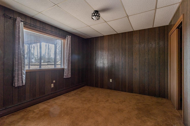 spare room featuring a drop ceiling, carpet flooring, wood walls, and baseboard heating