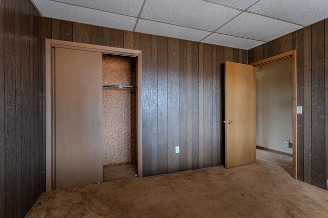 unfurnished bedroom with wooden walls, a paneled ceiling, a closet, and carpet floors