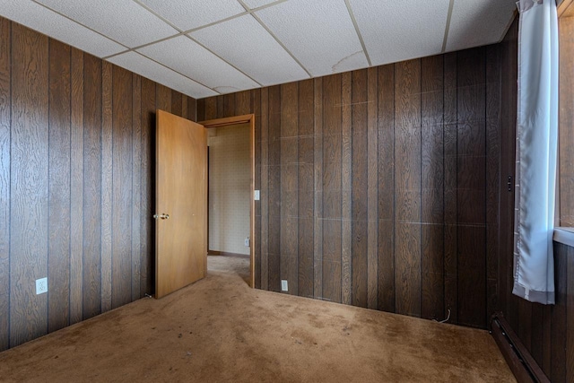 carpeted empty room with a baseboard heating unit and wood walls