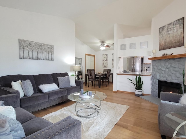 living room featuring high vaulted ceiling, a ceiling fan, wood finished floors, a fireplace, and baseboards