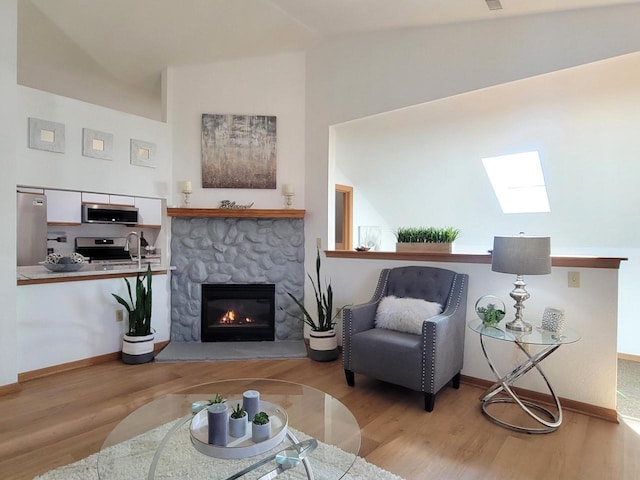 living room with a stone fireplace, lofted ceiling with skylight, wood finished floors, and baseboards